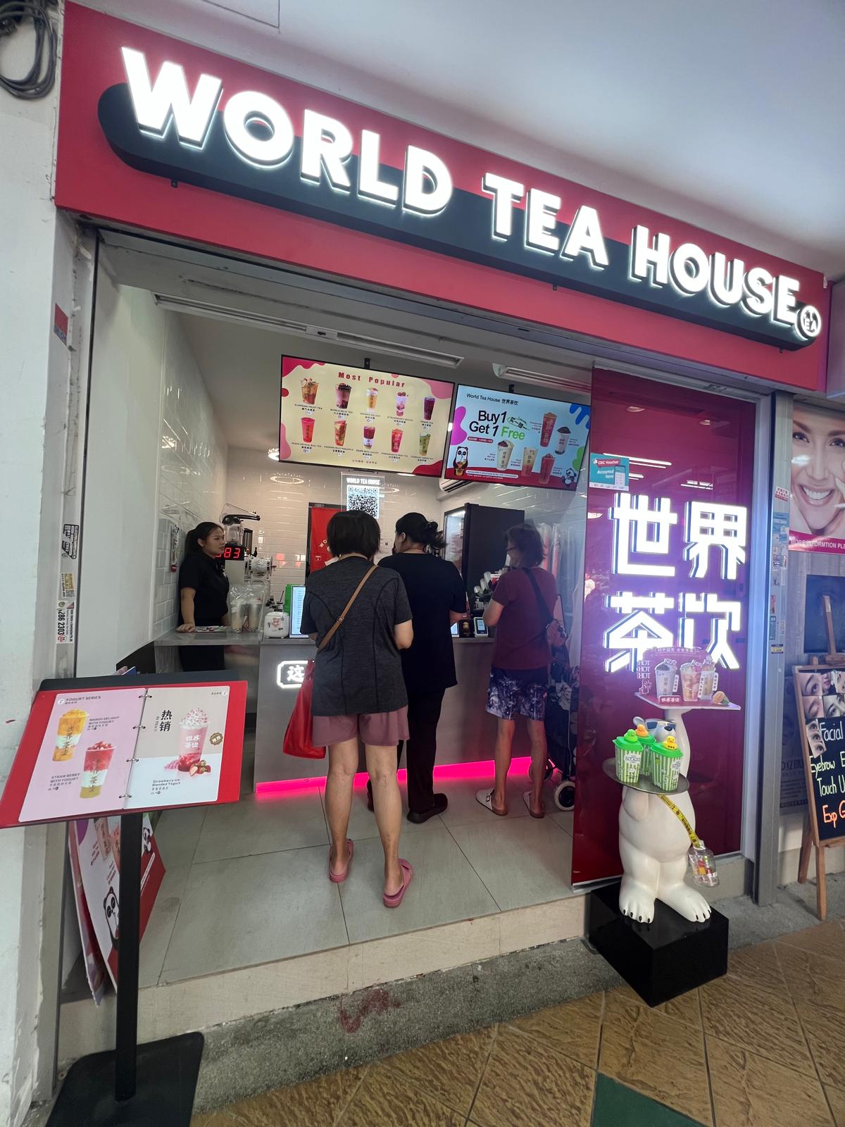 Full storefront exterior of World Tea House showing glowing overhead main sign, store entrance, and customer ordering area