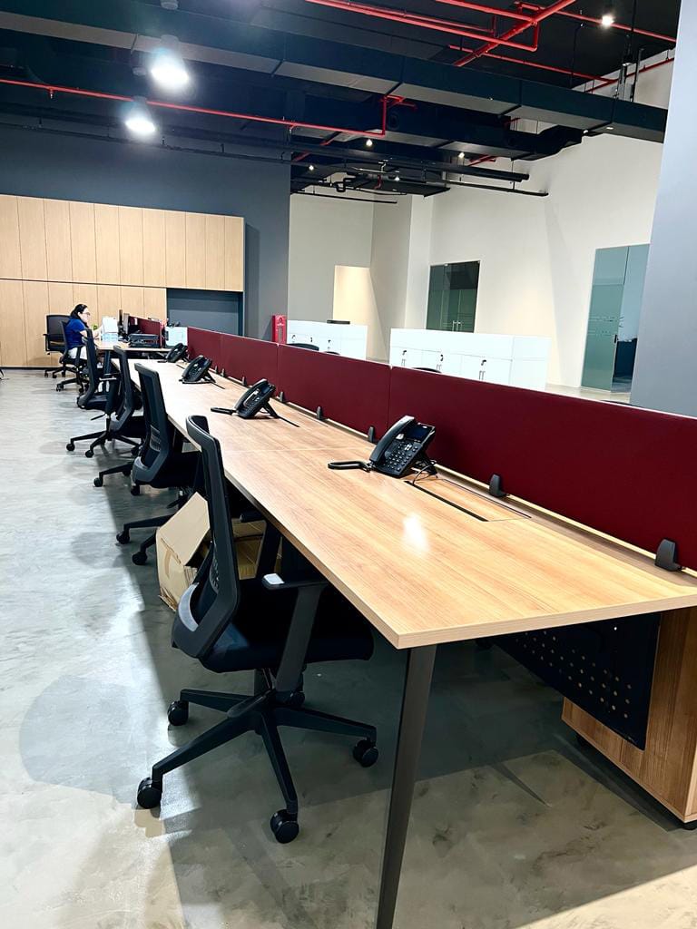 leinteri-gourmet-partner-partition-open-desks Long open-plan office desk cluster with maroon privacy divider screens, desk phones, and screed floor