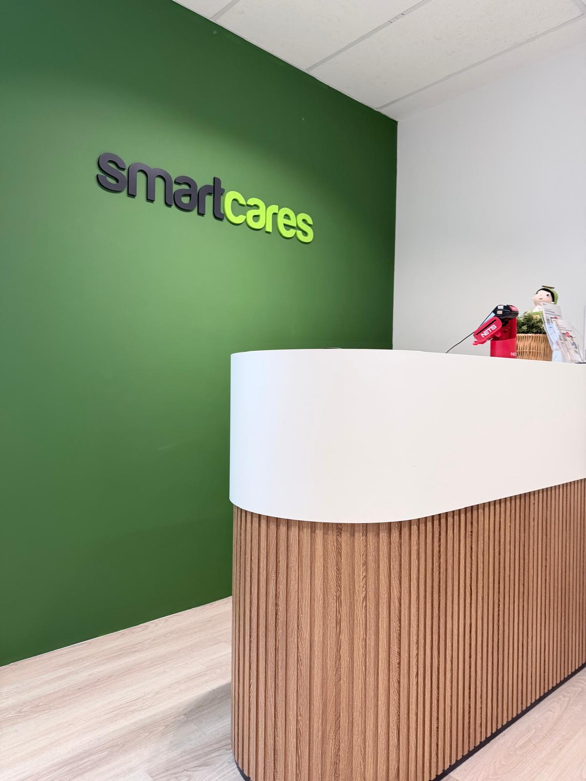 Green feature wall displaying raised 3D acrylic SmartCares brand signage above the front desk.