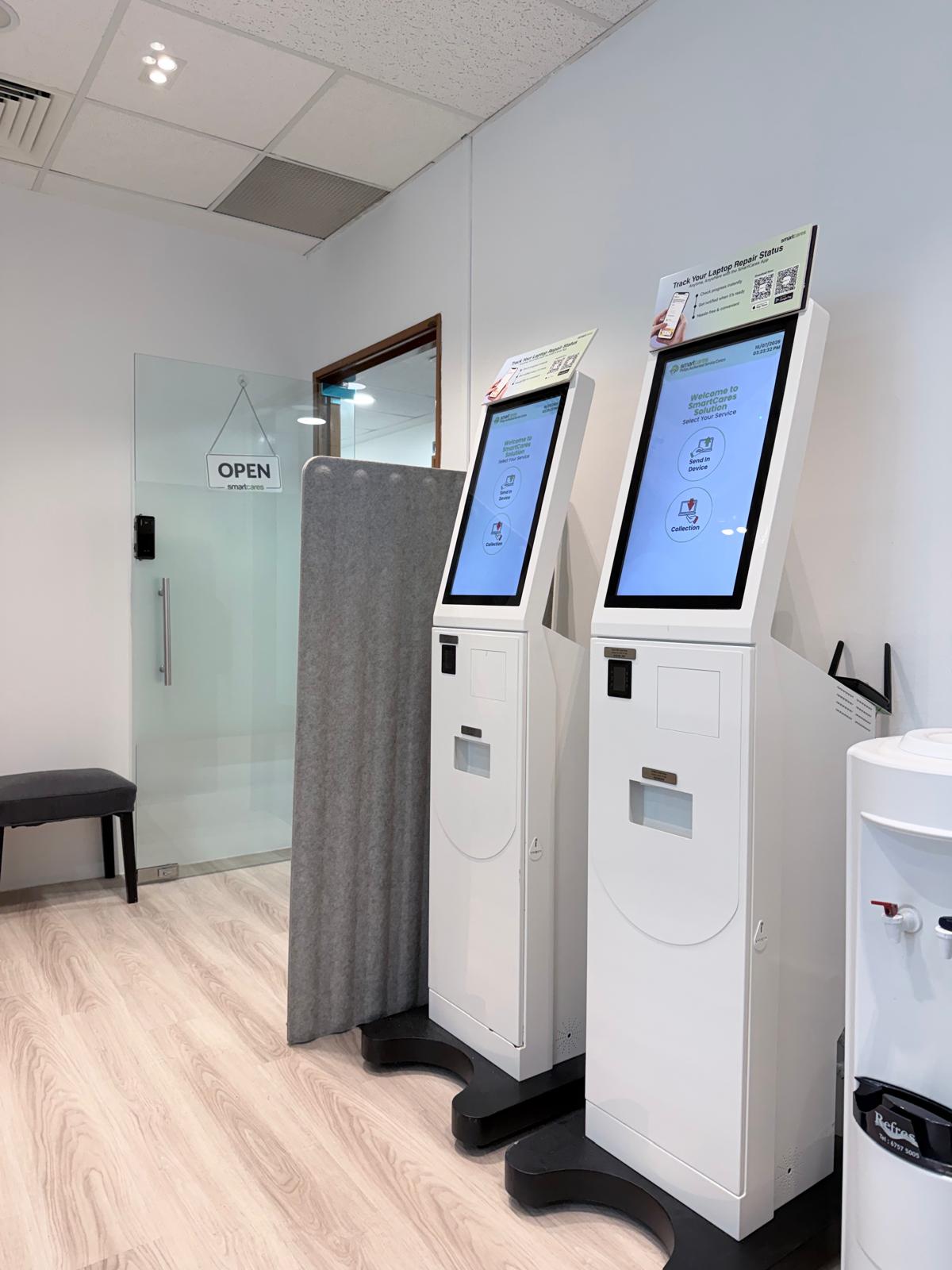 leinteri-smartcares-service-kiosks-entrance Two white automated customer service kiosks standing near a glass entrance door.